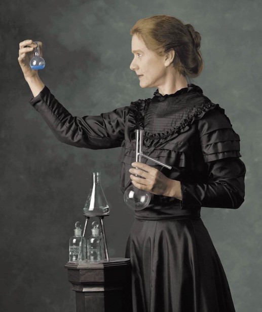 Quadro de Marie Curie olhando e segurando com uma das mãos para um balão de fundo chato enquanto na outra mão segura um balão de distilação. Ao seu lado encontram-se outros equipamentos de química, colocados em um pedestal.
