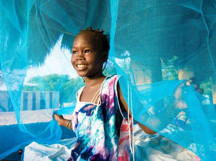 foto de uma menina sorridente segurando com as duas mãos as pontas de uma rede antimalária
