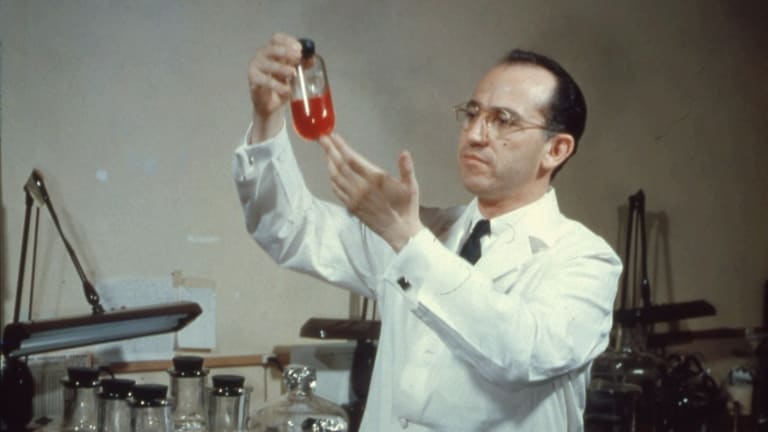 Jonas Salk em um laboratório, segurando um frasco de vidro vermelho
